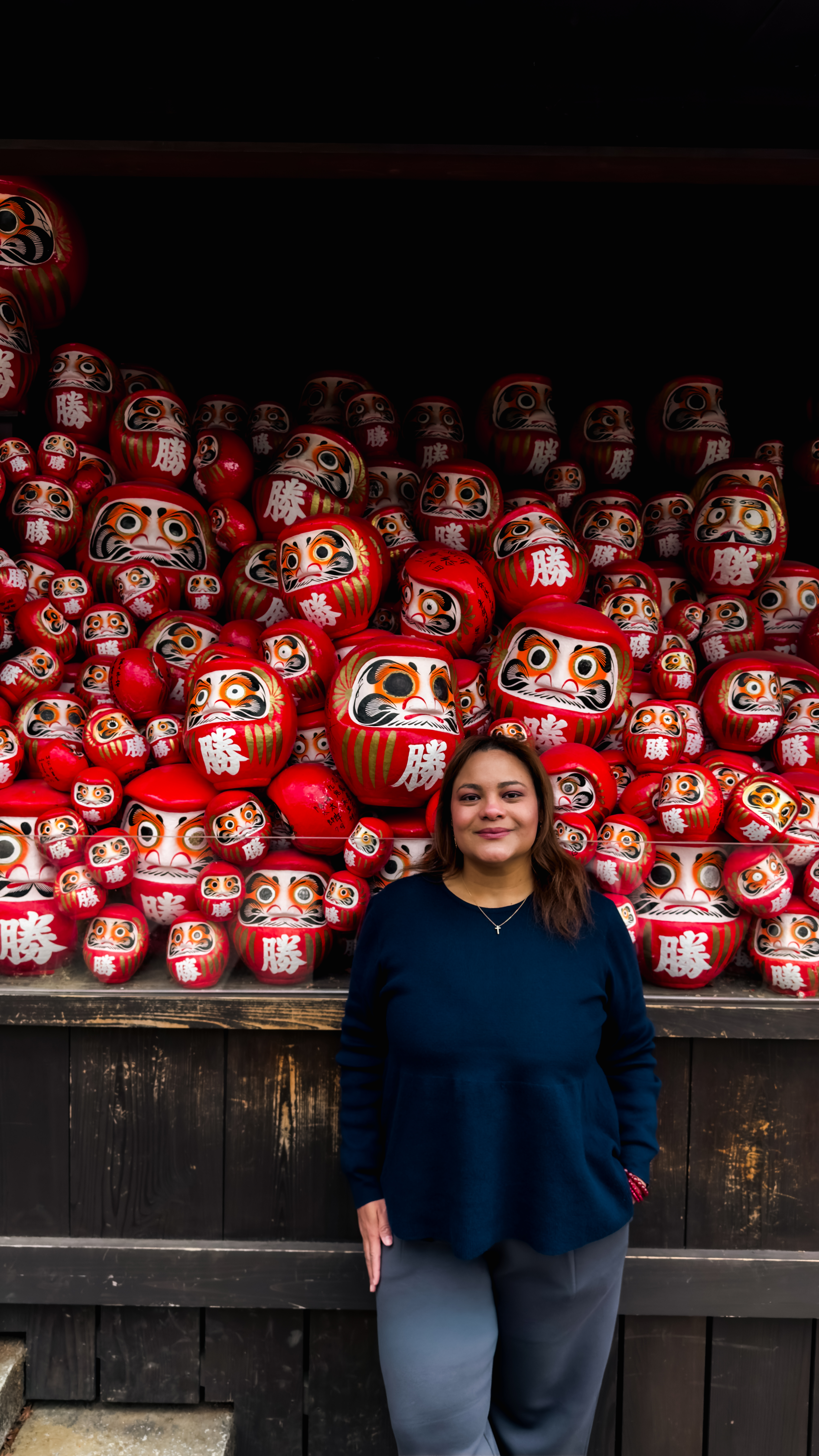Daniela frente a una colección de figuras Daruma en Japón